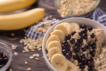 Bowl with tasty oatmeal, sliced banana and fresh berries on wooden table