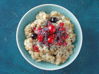 Bowl with tasty oatmeal, berries and poppy seeds on color textured background