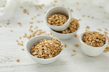 Bowls with raw oatmeal on light background