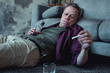 Smoking man. Drunk exhausted man looking not pleasant at all while smoking cigarette lying on the floor