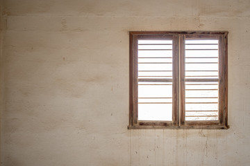 Fototapeta premium A glassless, barred window in the wall of a room in an abandoned, derelict building with stained walls.