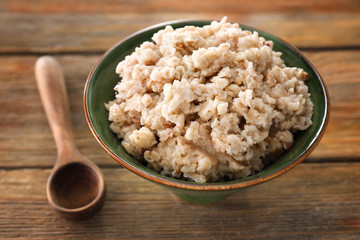 Bowl with tasty oatmeal on wooden background