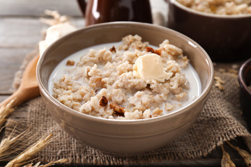Bowl with tasty oatmeal and milk on wooden table