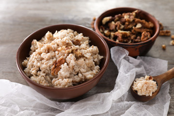 Bowls with tasty oatmeal and walnuts on wooden table