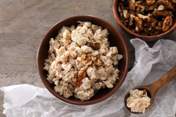 Bowl with tasty oatmeal and walnuts on wooden table