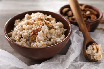 Bowl with tasty oatmeal and walnuts on table