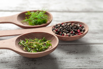 Spoons with different fresh herbs and spices on wooden background, closeup