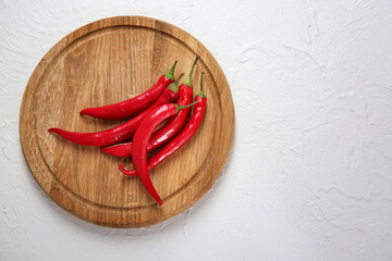 Wooden board with fresh chili peppers on light background