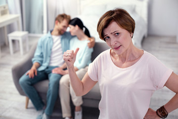 My son is there. Depressed senior woman feeling unhappy while pointing at her son and his wife