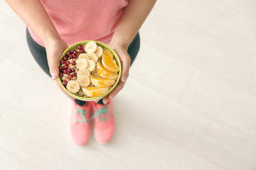 Sporty young woman with bowl of tasty oatmeal indoors