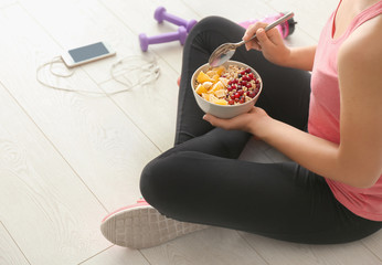 Sporty young woman sitting on floor with bowl of tasty oatmeal