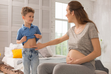 Pregnant mother. Handsome cute curly son feeling loved while looking at tummy of his beautiful pregnant mother