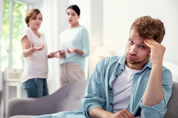 I want peace. Sad cheerless man listening to his wife and his mother while being tired from quarrels