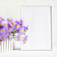 Front view blank mock up of photo frame on the white background. Purple flowers on a white wooden table background with copy space. Home floral interior. 