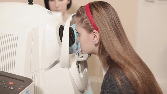 Side view shot of young girl having her eyes examed on eye tomography machine in hospital. Ophthalmologist's office.