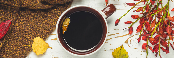 Mug of hot coffee in autumn setting on a wooden table with a knitted scarf, sweater. Comfort, warmth, cozy.. Banner