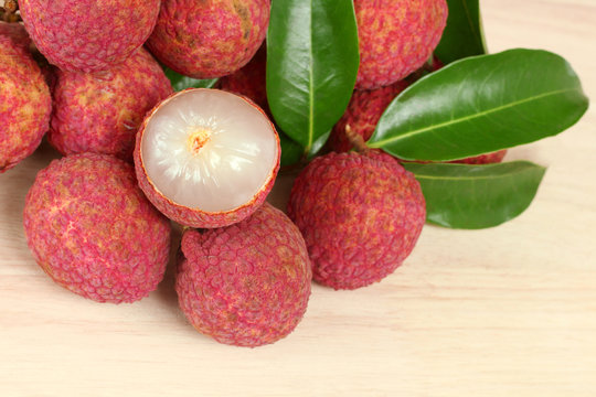 Fresh red lychee and peeled with leaves on wooden background with copy space.