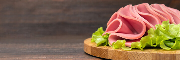 Sliced sausages with salad leaves on the wood background. Banner