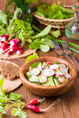 Fototapeta na wymiar Lenten spring vegetable salad from cucumber, radish, greens and oil in a wooden plate