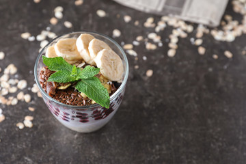 Tasty oatmeal dessert with fresh berries, sliced banana and flax seeds in glass on grey table