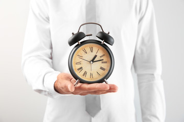 Businessman holding alarm clock on light background, closeup. Time management concept