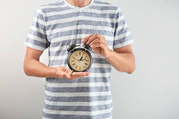 Man holding alarm clock on light background. Time management concept