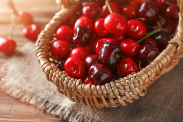 Wicker basket with ripe cherry on wooden background, closeup