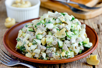 Meat salad with fresh cucumber, marinated mushrooms, boiled eggs and dill in clay plate on wooden...