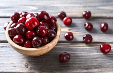 Bowl with ripe cherry on wooden background