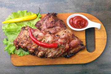 grilled barbecued ribs with lettuce leaves, hot chili pepper and sauce on wooden cutting board.