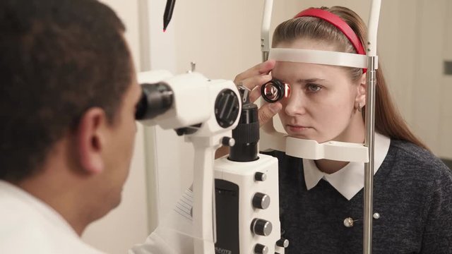 the oculist doctor works in a private clinic, the man uses an apparatus for biomicroscopy of the eye to check the sight of an adult teenager