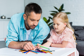 father and daughter drawing with colored pencils together at home