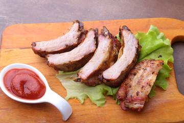 grilled barbecued ribs with lettuce leaves, hot chili pepper and sauce on wooden cutting board.