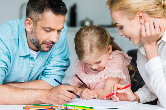 parents with cute little daughter drawing with colored pencils together at home