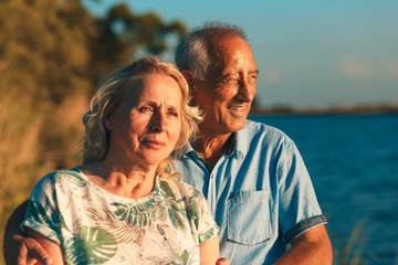 Portrait of happy senior couple by the lake on sunny day.
