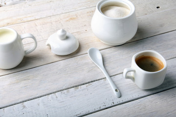 Cup of hot coffee espresso, coffee beans, jug of milk, and bowl with sugar on white background for copy space. Coffee concept.