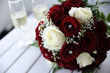 Beautiful red and white roses wedding bouquet on a table with two champagne flutes