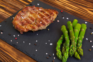 Grilled beef steak and asparagus on wooden background