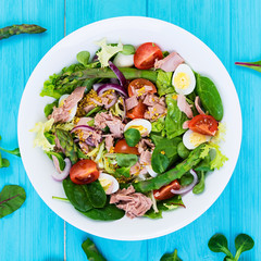 Salad with tuna, tomatoes, quail eggs, asparagus and onions on wooden background