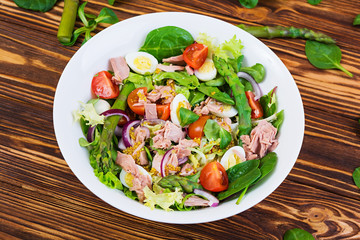 Salad with tuna, tomatoes, quail eggs, asparagus and onions on wooden background