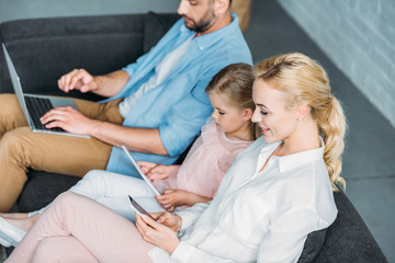 high angle view of parents with cute little daughter sitting on couch and using digital devices