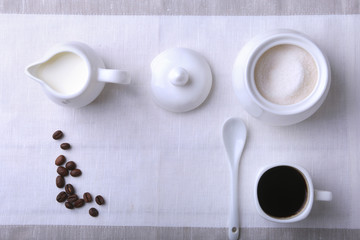 Fototapeta na wymiar Cup of hot coffee espresso, coffee beans, jug of milk, and bowl with sugar on white background for copy space. Coffee concept.