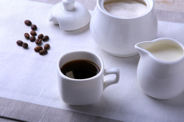 Cup of hot coffee espresso, coffee beans, jug of milk, and bowl with sugar on white background for copy space. Coffee concept.