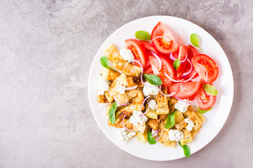 Fried zucchini with feta cheese, tomatoes, herbs and onions on a plate on a table. Top view. Copy space
