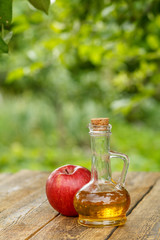 Apple vinegar in glass bottle and fresh red apple on wooden boards with green natural background