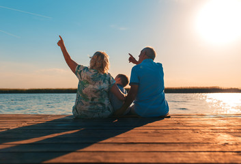 Grandparents with grandson enjoying time together by the lake. - obrazy, fototapety, plakaty