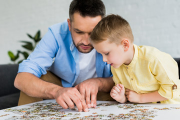 focused father and son playing with jigsaw puzzle together at home