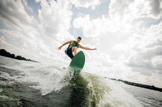 Young attractive man riding on the green wakeboard