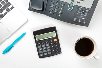 Conceptual workspace or business concept. Laptop computer with cup of coffee, blue pen and modern IP phone and calculator on white background. Top view