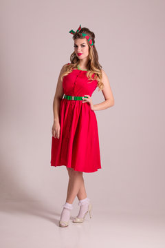 Pretty girl in red dress with hairdo stands in grey studio, pin up style
